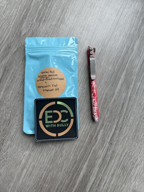 Blue resealable bag with a round handwritten label, a black 'EDC with Sully' card, and a glittery red utility knife on a gray wood surface.
