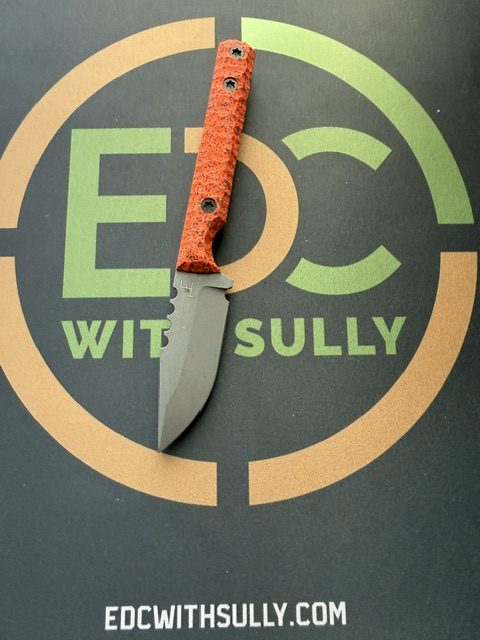 Orange-handled knife rests on a dark surface featuring the 'EDC with Sully' logo and website.