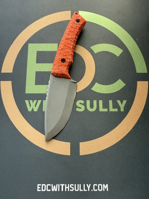 Orange-handle folding knife placed on an EDC with Sully logo backdrop. Highlighting the knife as a product photo for review or sale.